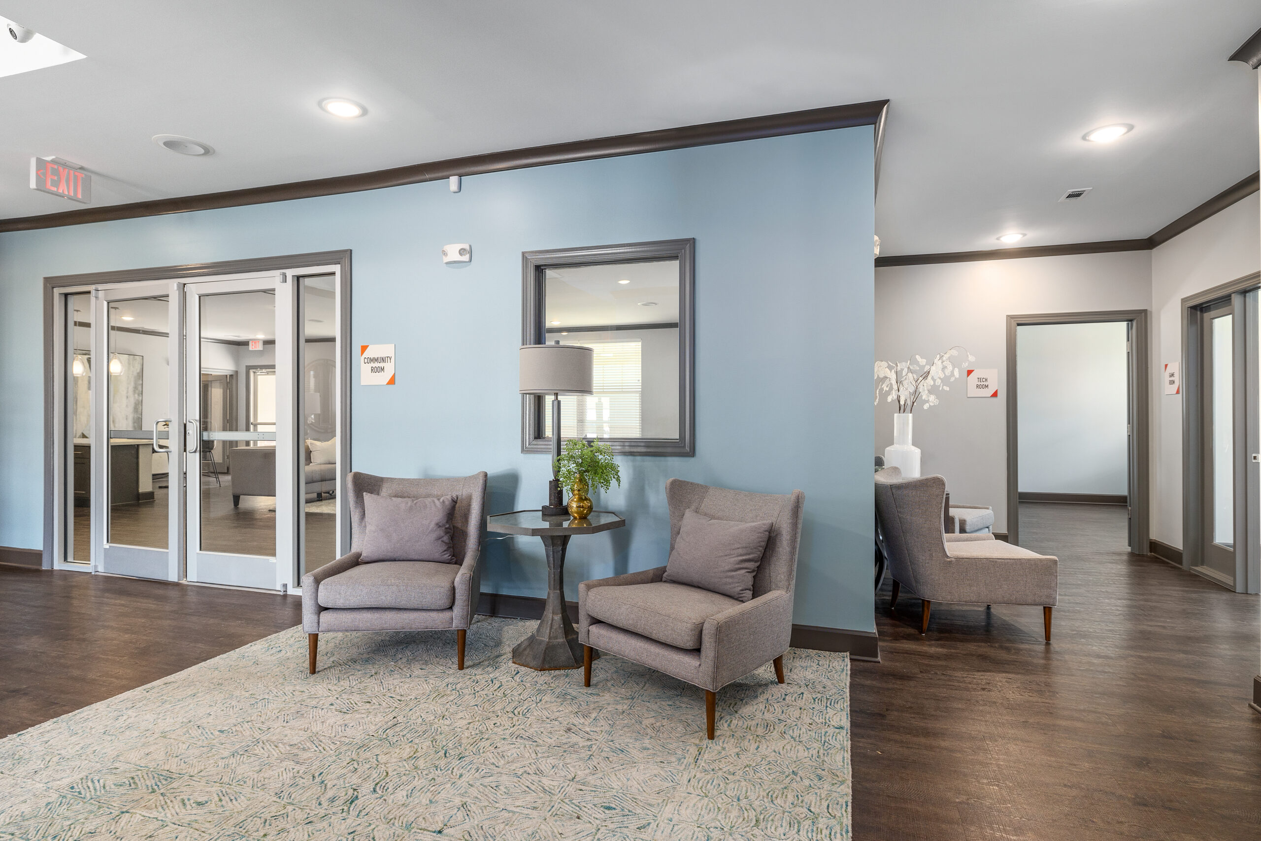 Community room at Le Jolliet featuring two comfy grey chairs and a small table in between them with modern decor.