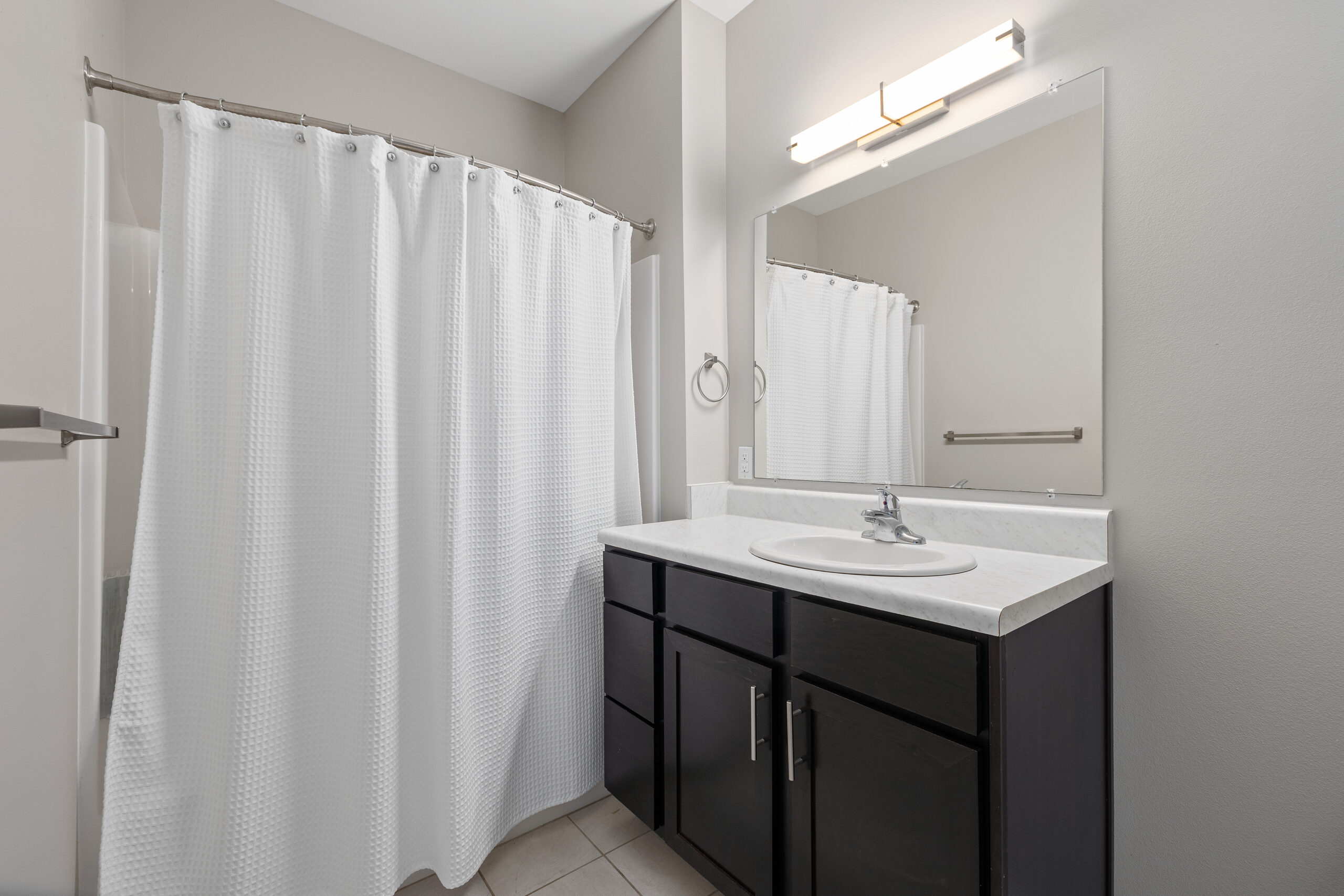 A bright bathroom featuring a white shower curtain and a sleek vanity under a large mirror at Le Jolliet Apartments.