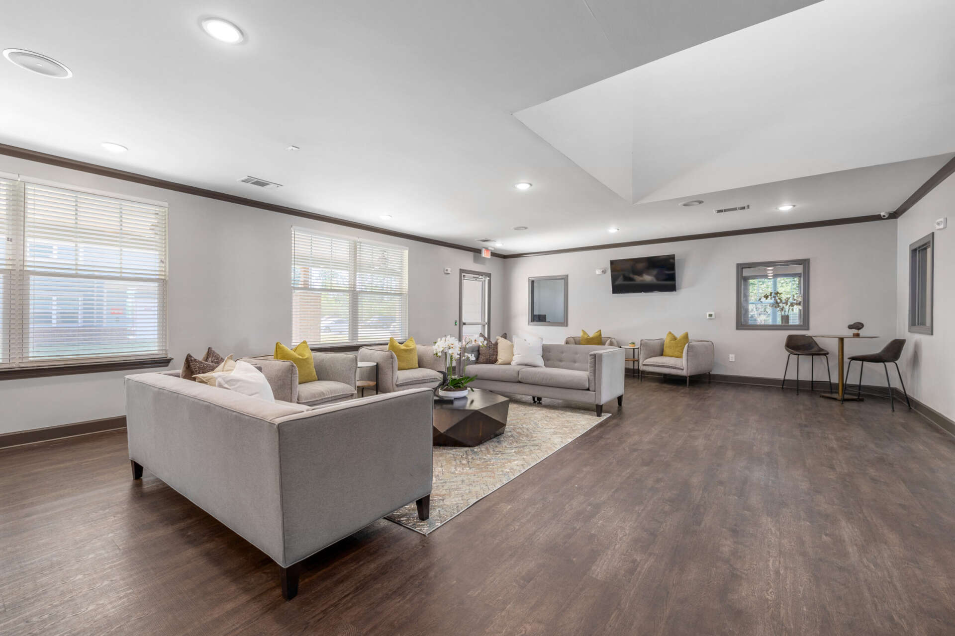 Spacious community room at Le Jolliet Apartments featuring hardwood flooring, three grey couches, and two grey chairs.